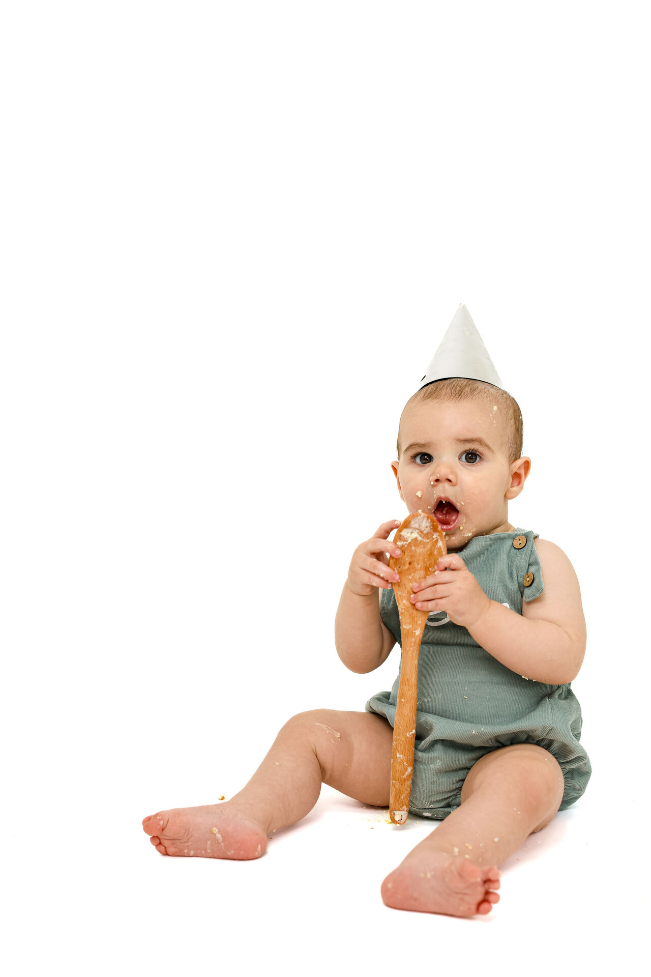 Baby in party hat holding a wooden spoon during a cake smash shoot